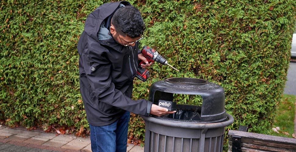 A city worker installs a Pello smart sensors to public realm garbage and recycling bins across Vancouver to track fill rates and service patterns