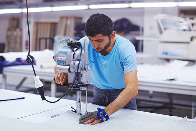 A male Vancouver apparel and fashion industry worker in a textile shop using a industrial sewing machine.