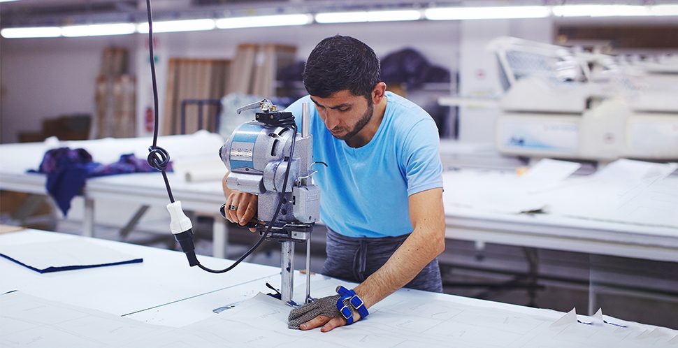 A male Vancouver apparel and fashion industry worker in a textile shop using a industrial sewing machine.